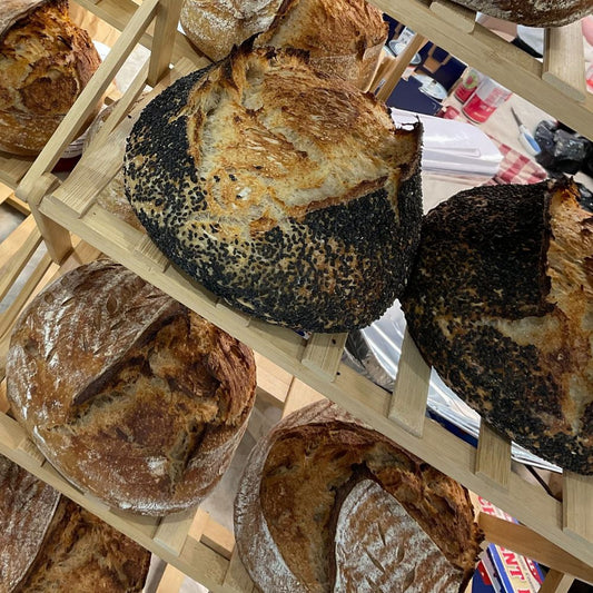 Assorted loaves of bread on a wooden rack with a magazine in the background.