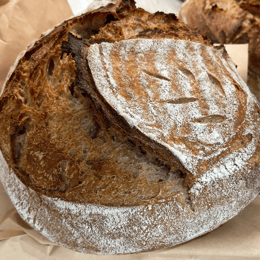 Loaf of bread with a slice cut off, dusted with flour, on a brown paper background