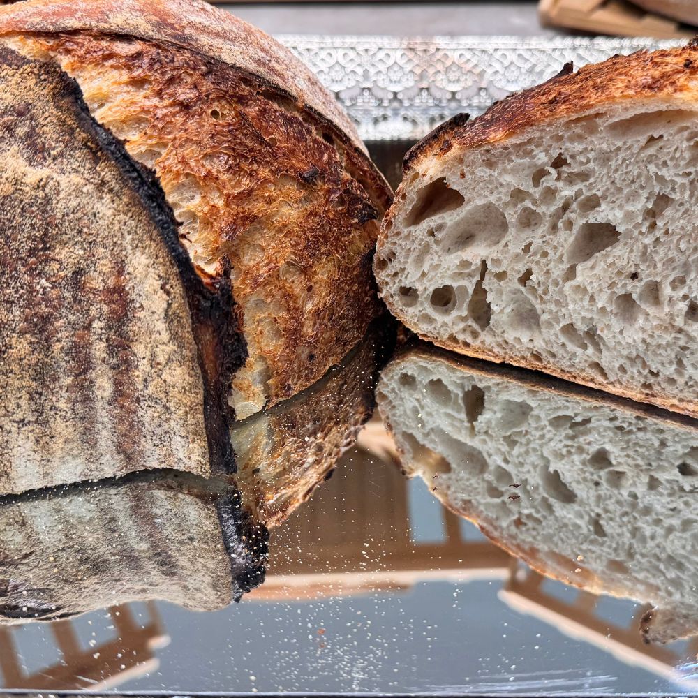 Close-up of a loaf of bread with a slice cut off, on a reflective surface.